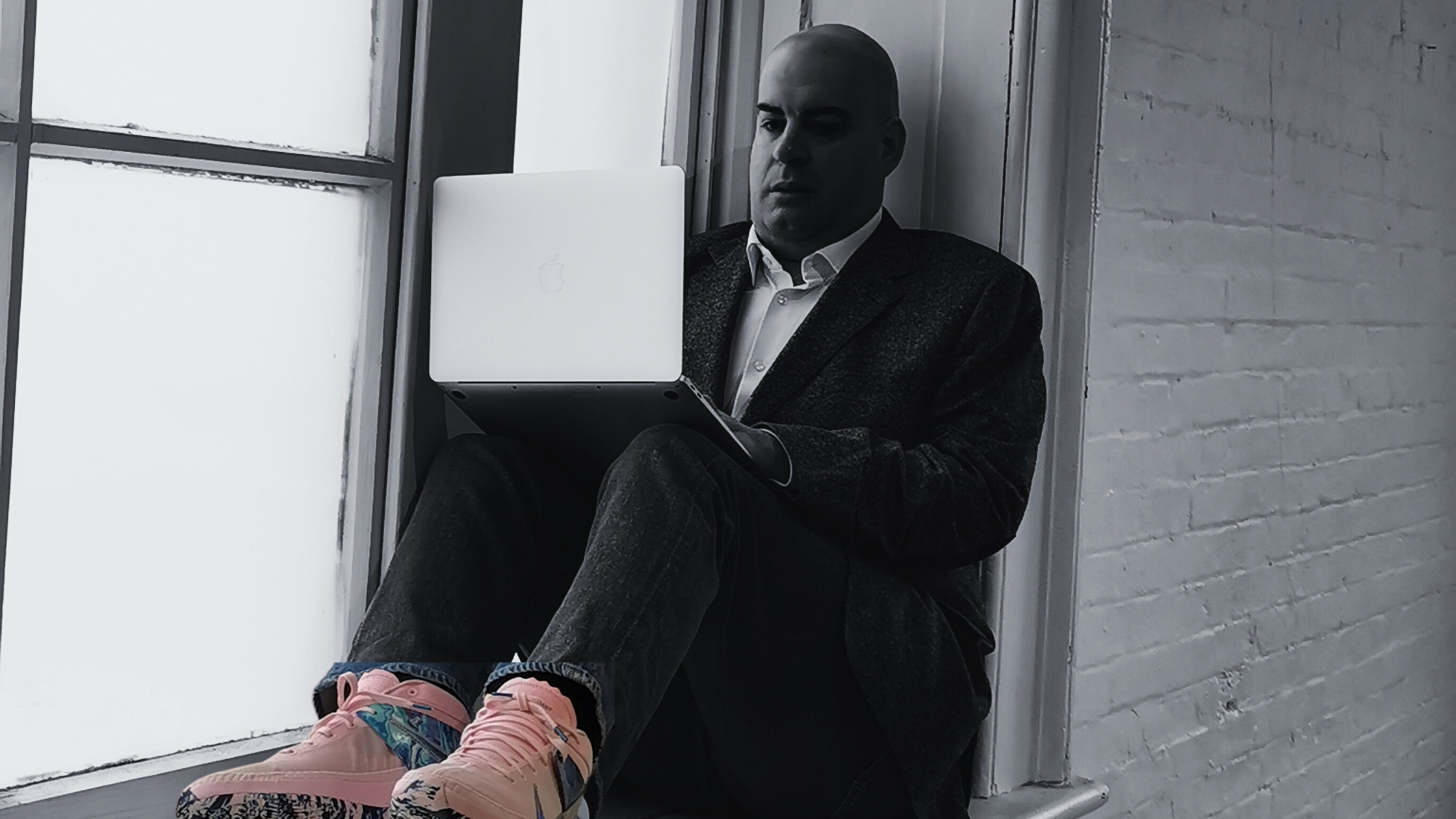 Man sitting on a window sill using a laptop computer. His shoes are pink.
