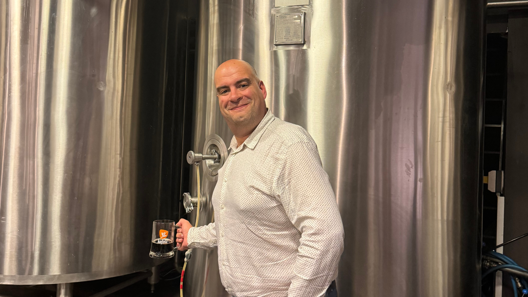Richard Liverman stands by a tall stainless steel dispenser. He holds a beer glass.