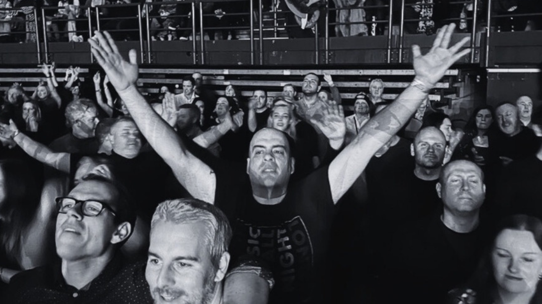 Black and white image of a man in a concert hall. A man is the centre reaches he arms up.